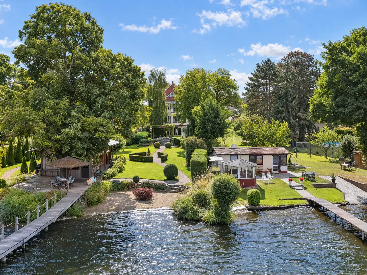 Drohnenaufnahme eines Seegrundstücks mit Garten und Stegen Nach der Bearbeitung.