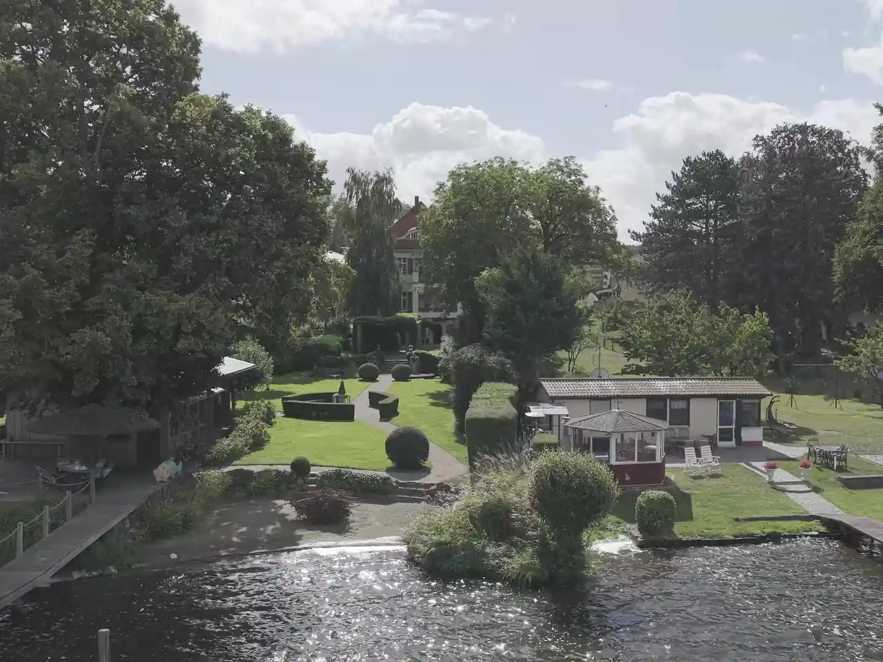 Drohnenaufnahme eines Seegrundstücks mit Garten und Stegen Vor der Bearbeitung.